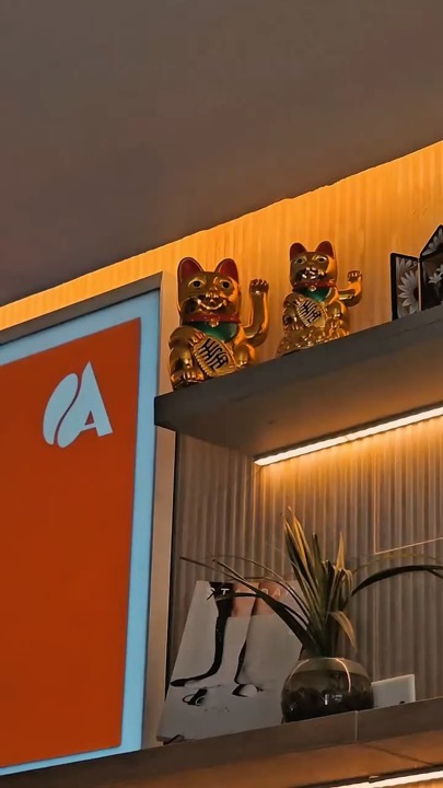 Repisa con gatos de la suerte y el logo de Antaqa en la cafetería